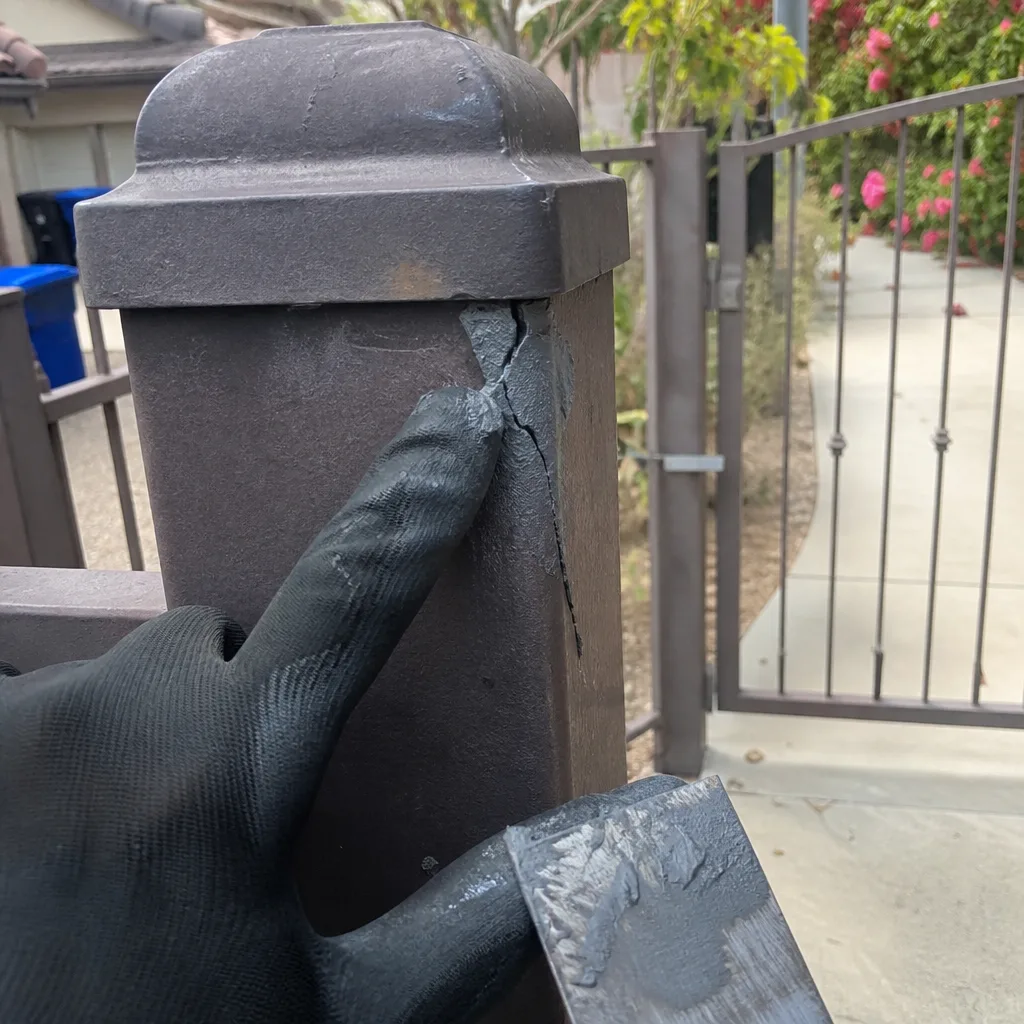 Gloved hand inspecting damage on a metal gate post for repair